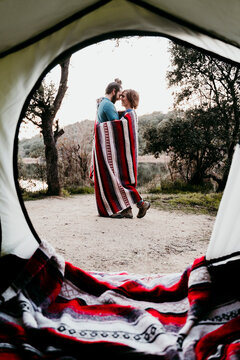 Couple wrapped in a blanket camping at lakeside