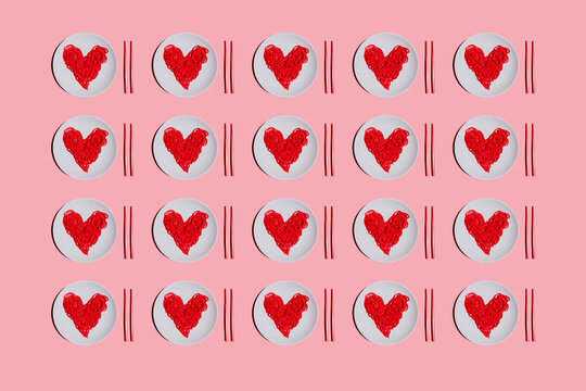 Pattern of plates with red-colored heart-shaped spaghetti against pink background