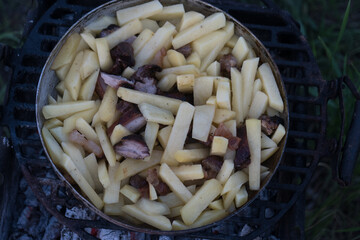 jacket potatoes, squash and sausages are cooked in a large frying pan on an open fire