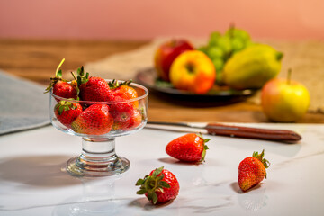 strawberries in a glass bowl on a background of apples, lemon and grapes