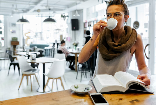 Woman reading book in coffee shop drinking coffee