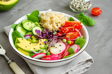Quinoa salad with fresh vegetables, spinach, green peas, microgreens and sesame seeds in a bowl in a concrete background. Healthy food concept. Horizontal orientation.