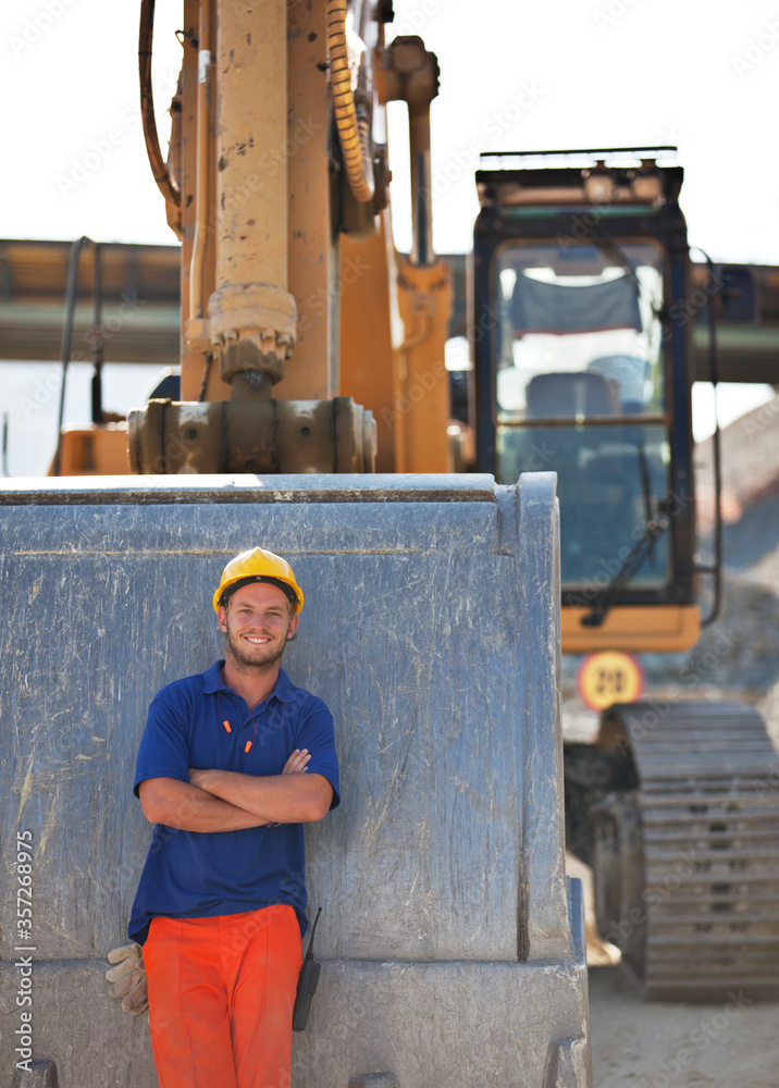 Wall mural Worker standing by digger on site