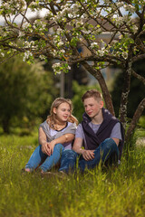 Fototapeta premium A young man and a girl sit under a blooming Apple tree