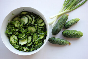 Summer fresh cucumber, dill, parsley, green onion salad in a white ceramic bowl on white wooden background. Top view 
