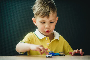 a boy in a bright T-shirt plays little cars at the table