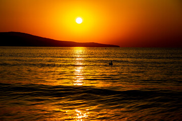 Fototapeta na wymiar Beautiful orange view at sunrise, of the calm sea and sea coast with hills in the distance
