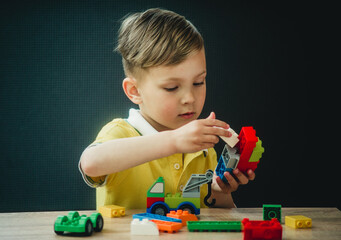 a boy in a bright T-shirt plays in a multi-colored designer at the table
