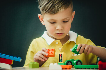 a boy in a bright T-shirt plays in a multi-colored designer at the table