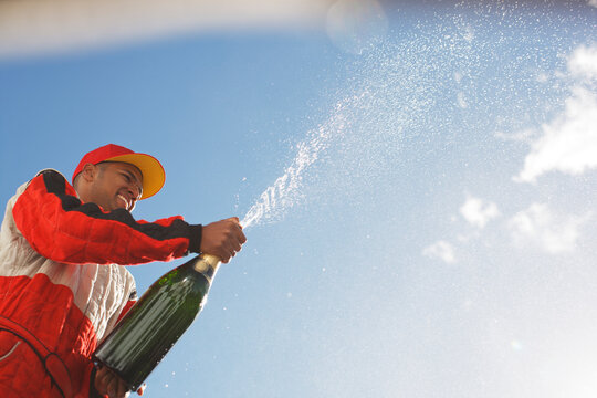 Racer Spraying Bottle Of Champagne Outdoors