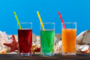 Fresh orange fruit juice, reliable, strawberries stands on a wooden board right on the sandy sea beach.