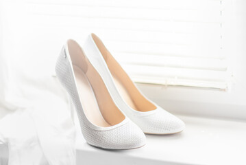 white shoes for the bride on a background of a bright window with jalousie