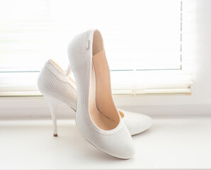 white shoes for the bride on a background of a bright window with jalousie