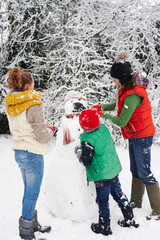 Mother and children making snowman outdoors