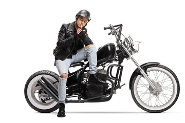 Fototapeta na wymiar Young biker with a helmet and a leather jacket sitting on a chopper motorbike and lighting a cigarette