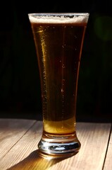 one glass of  lager beer on a wooden table on dark blured background