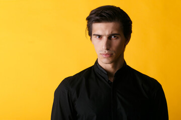 Handsome guy in black shirt over yellow background. Portrait of confident man.