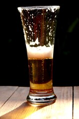 half a glass of light beer.  lager with foam on a wooden table on dark blured background