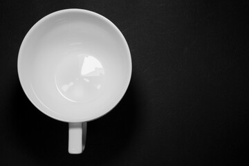 Top view of a big single round white tea cup with handle on a black table