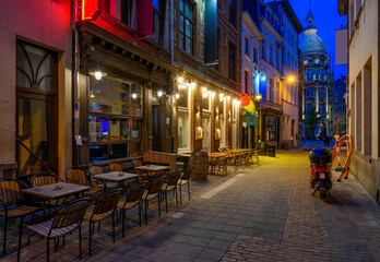 Old cozy narrow street with tables of restaurant in historic city center of Antwerpen (Antwerp), Belgium. Night cityscape of Antwerp. Architecture and landmark of Antwerpen