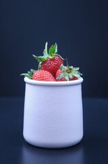 Ripe strawberries in a pot on a black background