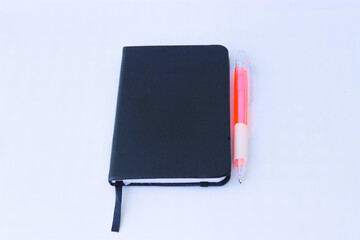 Black small notebook and plastic pen on a white background. Black leather notebook for notes. Transparent handle and pink plastic pen. for school, for office, study and work