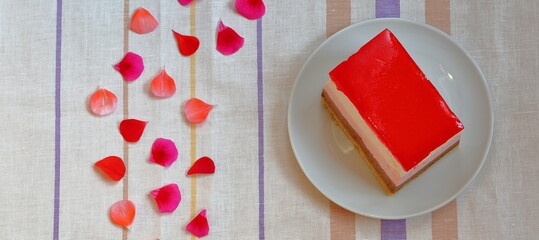 slice of cake with red gelatine at the top, petals decorate table top view