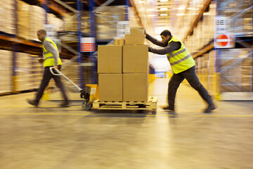 Workers carting boxes in warehouse - obrazy, fototapety, plakaty