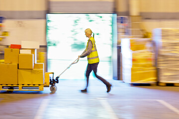 Blurred view of worker carting boxes in warehouse - obrazy, fototapety, plakaty