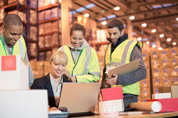 Businesswoman and workers using laptop in warehouse - obrazy, fototapety, plakaty