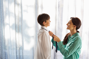 Mother tying son's tie at window