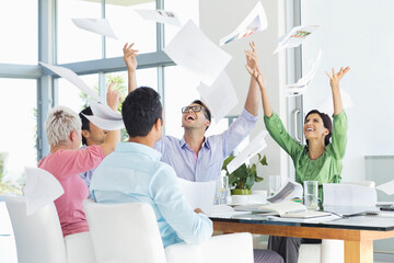 Business people tossing papers in air in meeting - Powered by Adobe