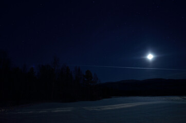 beautiful full moon lights up snowy winter field and star night sky