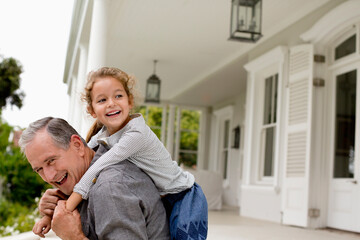 Older man carrying granddaughter piggy back on porch