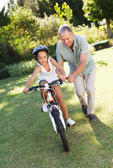 Obraz premium Older man teaching granddaughter to ride bicycle