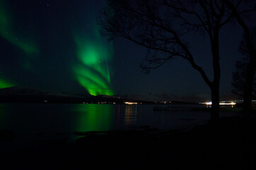 Naklejka na ściany i meble vibrant aurora borealis over fjord and mountain reflecting on fjord surface at night
