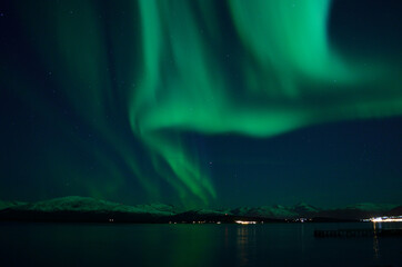 Fototapeta na wymiar incredible strong aurora borealis over fjord and snowy mountain