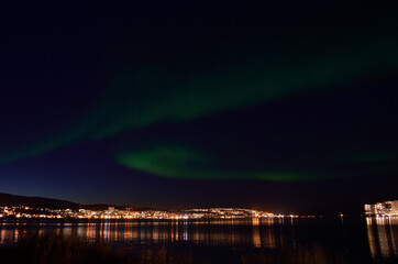 aurora borealis and city light reflection on fjord surface in autumn