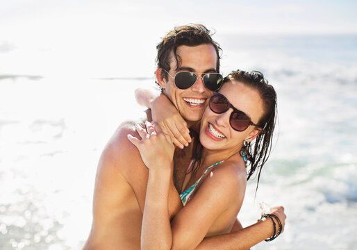 Portrait of enthusiastic couple in sunglasses hugging on beach