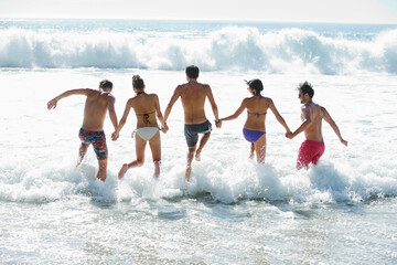 Friends holding hands and splashing in ocean