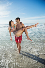 Fototapeta premium Man carrying woman in ocean surf