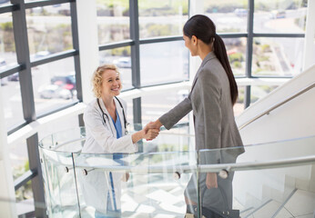 Doctor and businesswoman handshaking on stairs in hospital