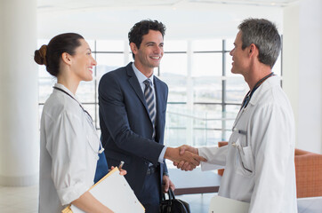 Doctor and businessman handshaking in hospital lobby