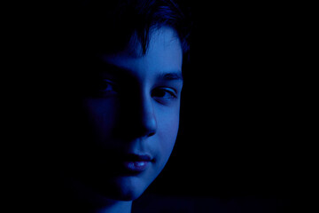 Portrait in blue of a teenager on a black background. The boy has dark hair