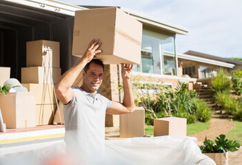 Man holding cardboard box overhead near moving van in driveway - obrazy, fototapety, plakaty
