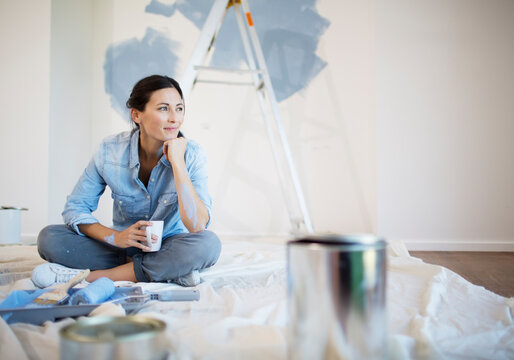 Woman relaxing with coffee among painting supplies