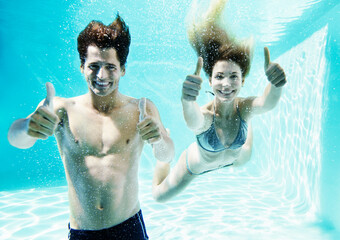 Couple giving thumbs up underwater in swimming pool