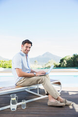 Man using laptop on lounge chair at poolside