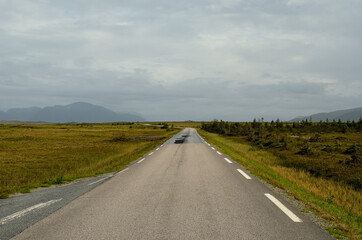 long road throug flat landscape with mountain and fog in backdrop