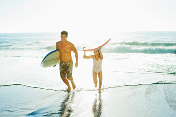 Father and daughter carrying surfboard and bodyboard on beach